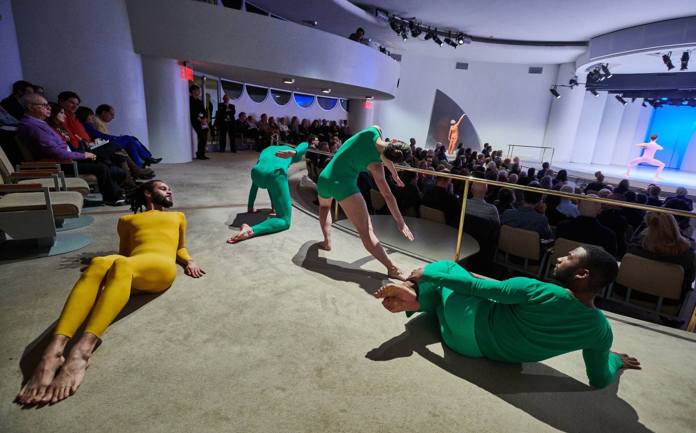 Three dancers in green and one in mustard yellow lounge in aisle